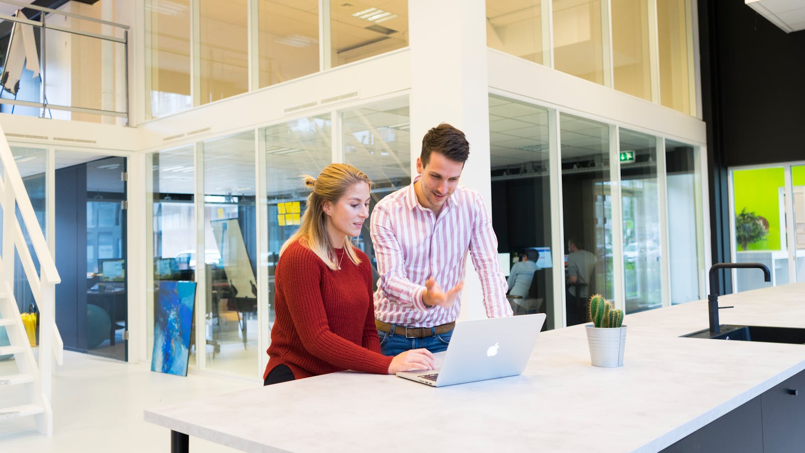 Two colleagues collaborating at a modern office with a laptop.